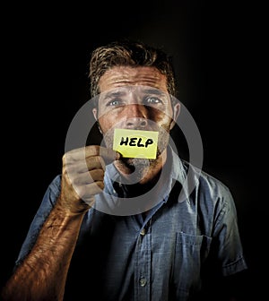 Dramatic portrait of young handsome and depressed man holding paper asking for help feeling sad looking miserable and frustrated s