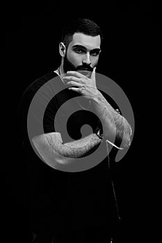 A dramatic portrait of a young serious guy, musician, singer, rapper with a beard in black clothes on a black isolated background