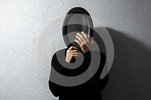 Dramatic portrait of young thoughtful guy, looking at his reflection in black oval mirror on textured wall of grey color.