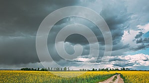 Dramatic Rain Sky With Rain Clouds On Horizon Above Rural Landscape Camola Colza Rapeseed Field. Country Road