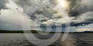 Dramatic rainy sky over a lake close to Soderhamn and Hudiksvall in Sweden. Dark blue stormy clouds and the sun shining through