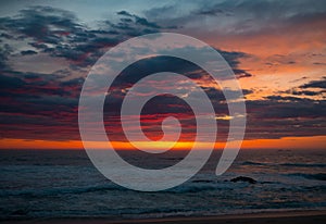 Dramatic red sunset sky with dark clouds over the ocean