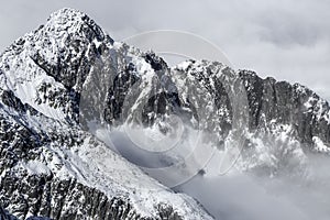 Dramatické, skalnaté, zasněžené pohoří, vrchol s mlhou, Vysoké Tatry, Lomnický štít, Slovensko, evropské alpy. Zblízka strmého útesu