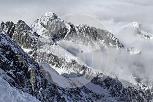 Dramatické, skalnaté, zasnežené pohorie, štíty s hmlou a oblakmi, Vysoké Tatry, Lomnický štít, Slovensko, európske Alpy.