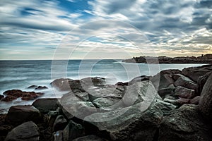 Dramatic seascape with stones on the shore. Long exposure. Blurred water. Coast of the Atlantic Ocean.
