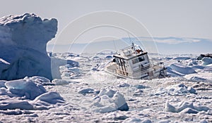 Dramatic shot of fishing boat crashing through the icefjord amongst large icebergs in Ilulissat, Greenland