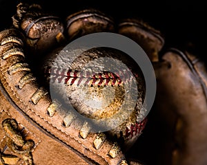Dramatic side lighting on old baseball caught in worn out mitt