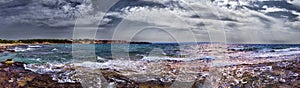 Dramatic sky and bad weather panoramic view at wild rocky bay  over sea with waves crashing at the shore with overcast rainy sky