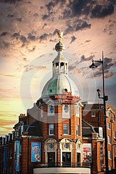 Dramatic sky over Wimbledon Theatre with golden sunset light illuminating the building's facade and dome