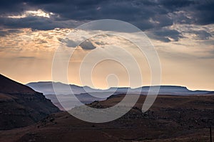 Dramatic sky, storm clouds and sun rays glowing over valleys, canyons and table mountains of the majestic Golden Gate Highlands Na