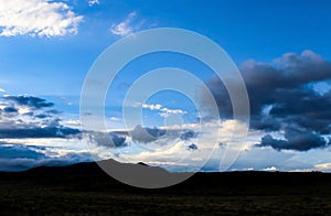 Dramatic skyscape over silhouette of mountains and flatland with stormclouds forming in very blue sky near dusk