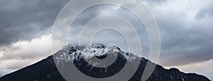 Dramatic snowy peak lonely mountain panorama landscape scenic moody view with cloudy gray sky background, copy space