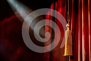 dramatic spotlight on gold tassel hanging from red stage curtain