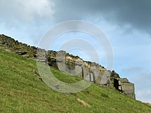 A dramatic stone outcrop on a steep green hillside in yorkshire moors landscape with the remains of an old dry stone wall