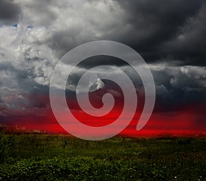 Dramatic stormy clouds and red sunset sky over green field