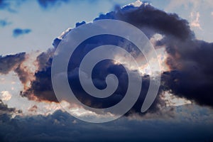 Dramatic stormy dark cloudy sky in bright rays of the setting sun at sunset.