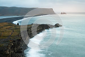 Dramatic stormy sunrise with clouds, fog and sunshine at scenic Kirkjufjara cliff looking to Reynisfjara black sand beach and Reyn