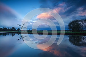 Dramatic stormy sunset over windmill by river