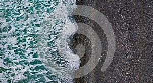 Dramatic stormy waves with white sea foam over black sand beach, aerial texture