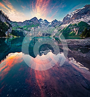 Dramatic summer sunset on unique lake - Oeschinen Oeschinensee, UNESCO World Heritage Site. Red clouds reflected in the calm sur