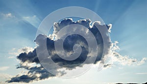 Dramatic sun rays breaking through a dark cloud in the blue sky.