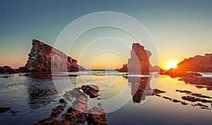 Dramatic sunrise with mist on the beach with rocks