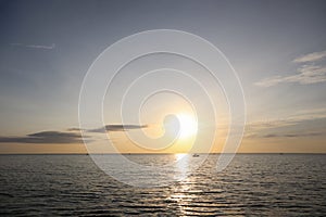 Dramatic sunrise ocean view with silhouette small boat and peaceful morning sky.