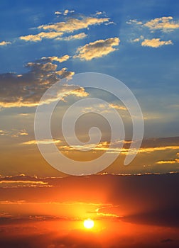 Dramatic sunset background with bright sun, blue sky and clouds