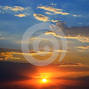 Dramatic sunset background with bright sun, blue sky and clouds