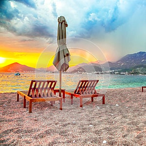 Dramatic sunset at beach with chaise lounges and umbrellas in Sveti Stefan near Budva