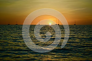 Dramatic sunset colours; beautiful sunset on a beach. Sun reflection in the water, with yacht silhouettes far away