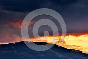 Dramatic sunset over the hill with forest, fiery clouds.