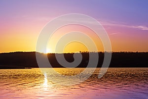 Dramatic sunset over river with orange and purple colors.Sun goes down over pond and forest silhouette. Beautiful nature backgroun