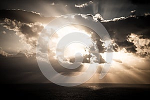 Dramatic sunset rays through a cloudy dark sky over the ocean