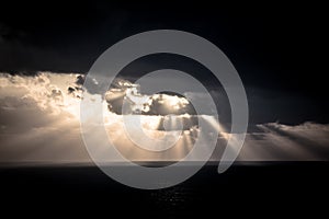 Dramatic sunset rays through a cloudy dark sky over the ocean