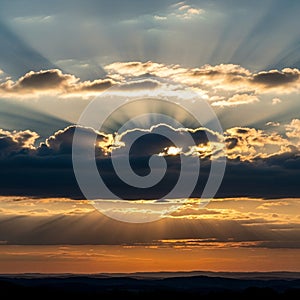 A dramatic sunset scene featuring sun rays streaming through scattered clouds,