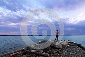 Dramatic sunset on the sea. The girl stands on the stone Bank