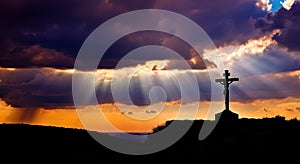 Dramatic Sunset Silhouette of Cross with Sun Rays Breaking Through Clouds