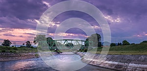 Dramatic sunset sky over old metallic railroad bridge and blurred motion river