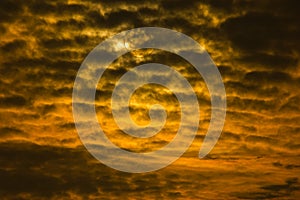 Dramatic sunset or sunrise with golden sky and black clouds forming a abstract with sun in the background.