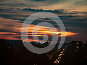 Dramatic sunset view over a modern city with illuminated building lights and orange sky