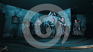 Dramatic theatrical dance performance with actors in period costumes on a dark, moody stage