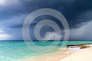 Dramatic view of dark grey storm clouds against the turquoise blue water of the Caribbean sea and a white sand beach