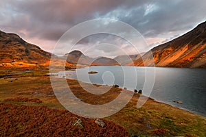 Dramatic view of Wastwater lake and mountains with golden evening light and dark clouds in sky. Lake District, UK.