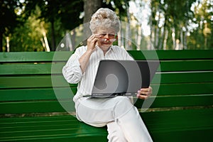 Drandma using laptop on the bench in summer park