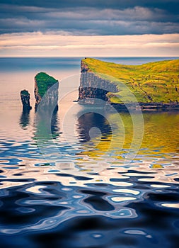 Drangarnir cliffs reflected in the calm waters of Atlantic ocean.