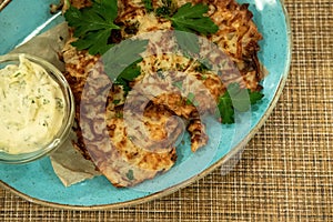 Draniki - potato pancakes on the blue plate served with sour cream and greens.