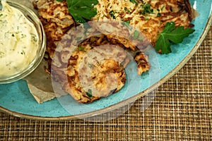 Draniki - potato pancakes on the blue plate served with sour cream and greens.