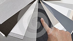 drapery catalog samples palette. architect's hand choosing samples of roller blind fabrics in different textures and colors.