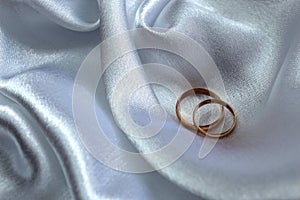 Gold wedding rings lie on satin fabric